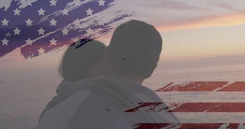 Couple embracing with us flag over ocean during sunset