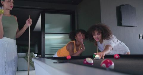 African american women playing pool and laughing in modern apartment game night