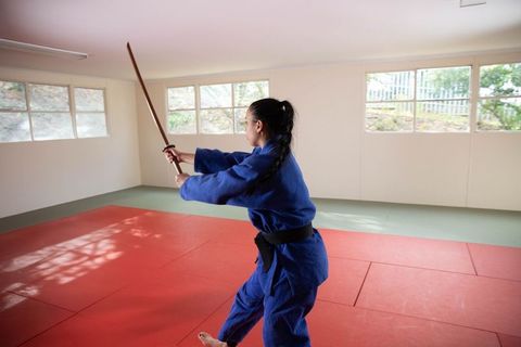 Asian woman practicing martial arts with wooden sword in minimalist dojo