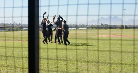 Baseball team celebrating victory in outfield through chain-link fence