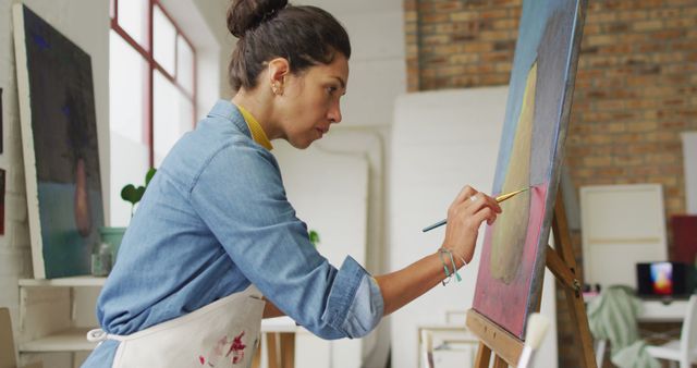 Young female artist painting on canvas in art studio, perfect for content about creative hobbies, art education, or highlighting the artistic process. Ideal for blogs, magazines, or social media posts focused on art, inspiration, and personal expression.