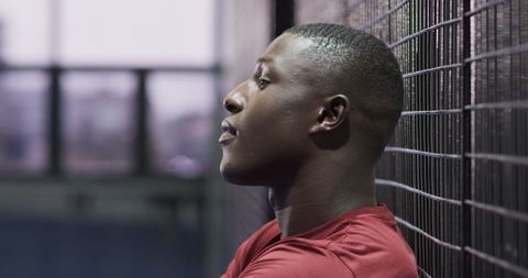 Pensive African American Athlete Leaning Against Fence in Gym