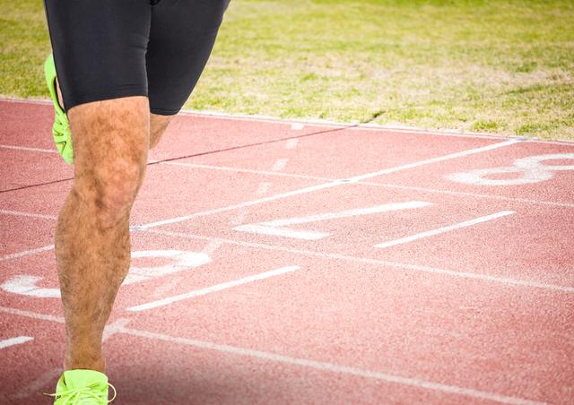 This image shows a close-up of a male athlete’s legs as he prepares for a race on a running track. He is wearing tight sportswear and bright shoes, emphasizing his readiness and focus. Ideal for use in articles or advertisements related to athletics, fitness, speed training, or sports competitions. Can be used in print or digital marketing to promote sporting events or athletic gear.