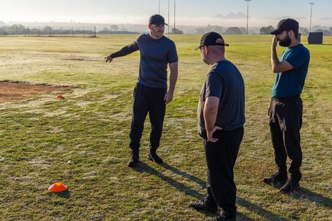 Coach leading morning field drill with diverse male players planning tactical training