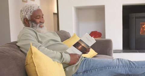 Elderly man reading book in cozy living room by fireplace