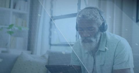 Senior man using tablet while wearing headphones and relaxing on couch at home