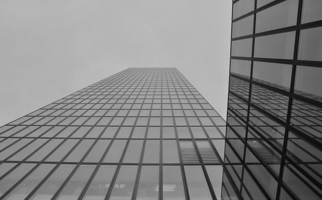 Ideal for corporate presentations, real estate websites, and architectural portfolios. This monochrome image showcases the sleek and modern design of a high-rise building with a glass facade, reflecting the sky and giving a sense of urban sophistication.