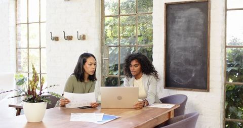 Female Professionals Collaborating with Charts and Laptop in Modern Office