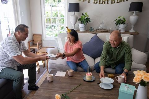 Asian family celebrating birthday at home with cake, gifts, roses and cozy living room