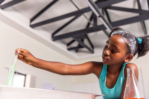African american girl conducting chemistry experiment wearing goggles in school lab
