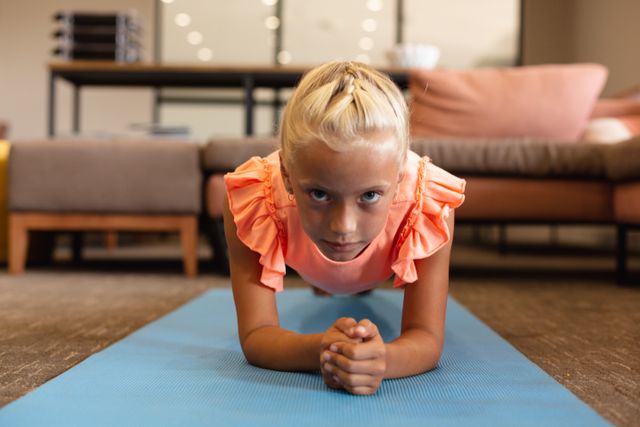 Portrait of caucasian elementary schoolgirl doing planks exercise on yoga mat in school. unaltered, childhood, education, yoga, exercising, activity and school concept.