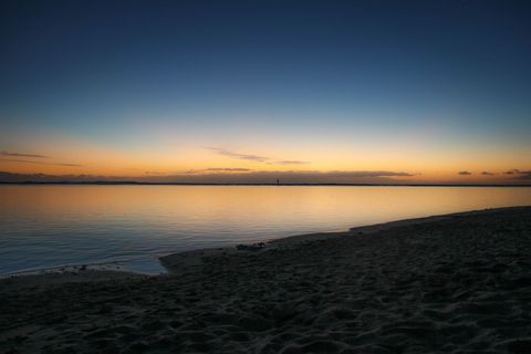 Tranquil Sunset Over Calm Coastal Bay with Sandy Shoreline and Reflective Water