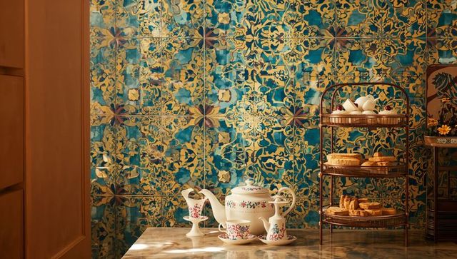Porcelain tea set with pastry stand on marble countertop against ornate blue teal gold tiles