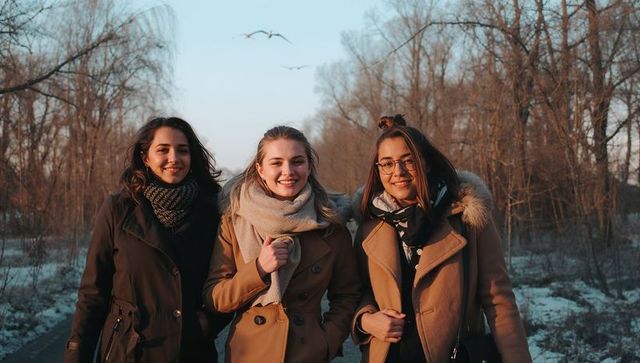 Three young women smiling on winter trail wearing coats and scarves in golden hour