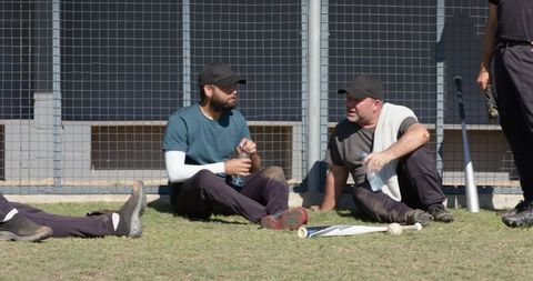 Baseball teammates resting on grass holding bats and water bottles after outdoor practice