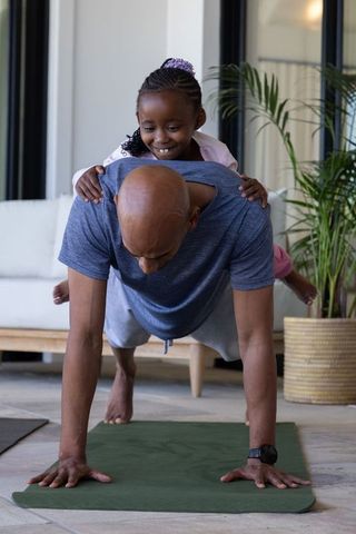 African american father holding plank while daughter riding on back during playful workout