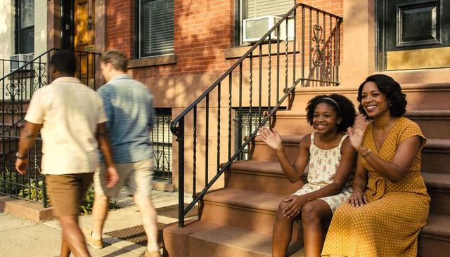 Mother and daughter sitting and waving on brownstone stoop in mustard and floral dresses