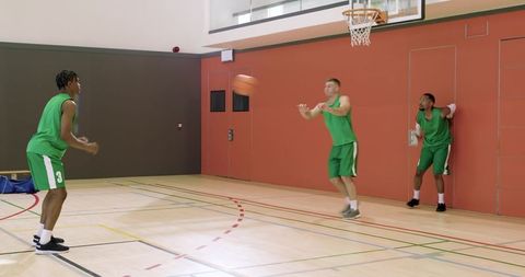 Diverse male basketball teammates practicing passing and layup drill on indoor court