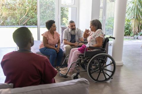 Multigenerational diverse family supporting senior woman in wheelchair during home visit