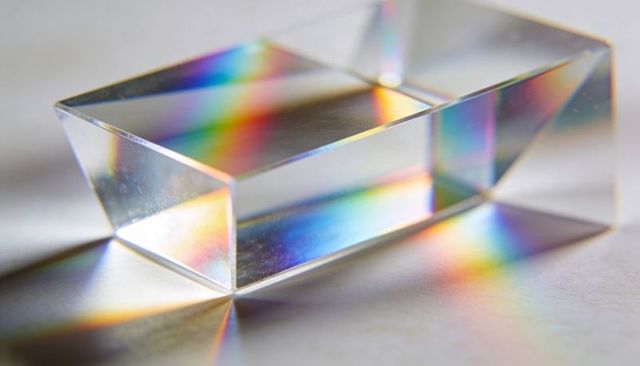 Clear rectangular prism casting rainbow spectra across white surface, glass reflections