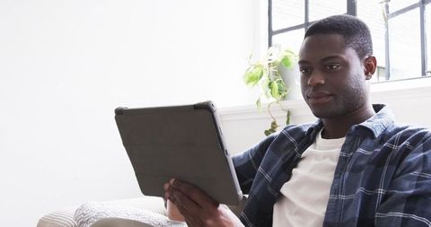 Man in casual attire using tablet near window with natural light