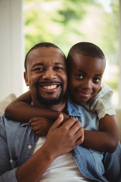 Father and son sharing a joyful moment at home, showcasing strong family bonds and affection. Ideal for use in family-oriented advertisements, parenting blogs, and lifestyle articles emphasizing the importance of family and togetherness.