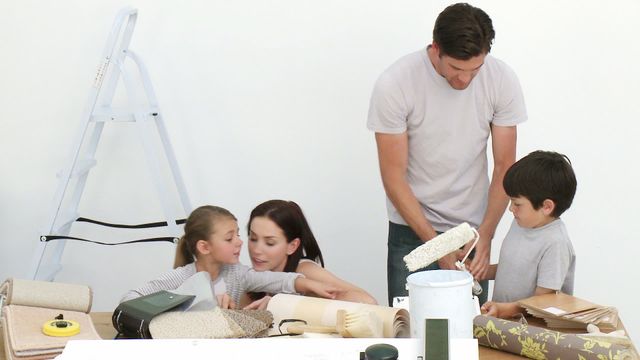 Parents and children work together in a room, surrounded by painting tools and wallpaper. This can be used for themes like family bonding, home improvement, DIY projects, teamwork, or interior design inspiration.