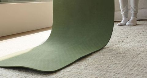 Rolling green yoga mat across sunlit carpet near window with mid adult male in socks