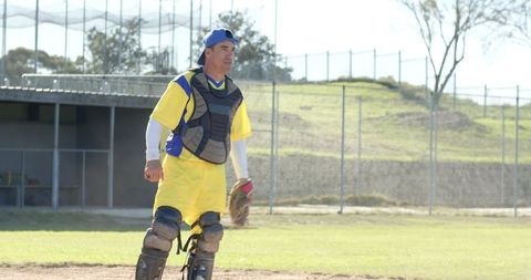 Mature catcher in yellow uniform standing on baseball field wearing full catcher gear and glove