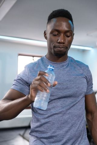 African american man holding water bottle and pausing during gym workout for hydration