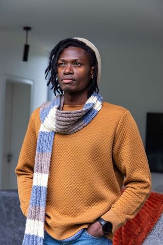 African american man standing in modern apartment wearing quilted sweatshirt and striped scarf