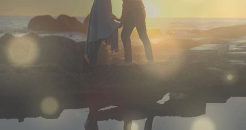 Couple holding hands on rocky jetty at sunset