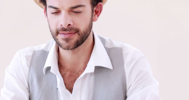 A young Caucasian man is focused on a task, wearing a casual white shirt with the sleeves rolled up, with copy space. His attire and demeanor suggest a relaxed work environment or a creative professional at work.