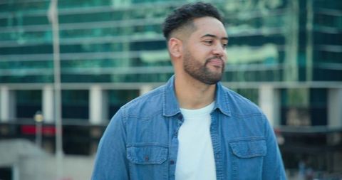 Young man standing in urban plaza wearing denim shirt and white tee turning right