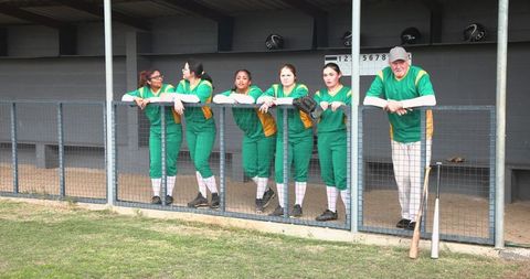 Female baseball team with coach leaning in dugout