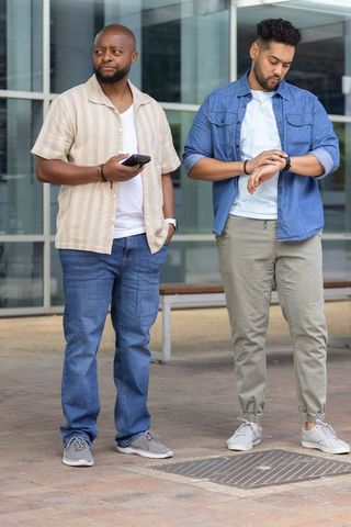 African american men waiting outdoors checking smartphone and smartwatch at urban plaza