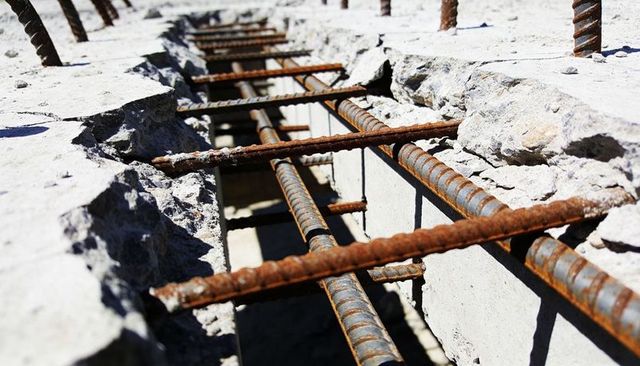 Revealing rusted ribbed rebar exposed in broken concrete slab showing corrosion and debris