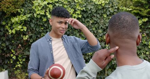 Young diverse men chatting in backyard holding football and showing stud earring