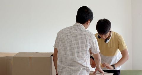 Father and son packing boxes together in bright living room