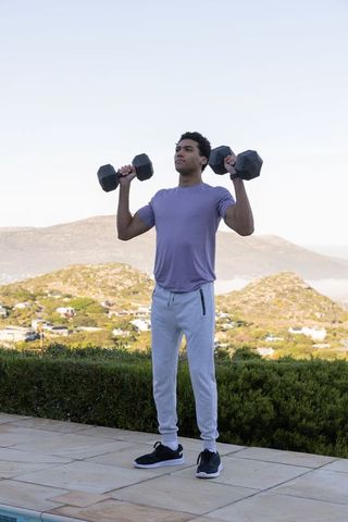 Man lifting dumbbells outdoors overlooking scenic landscape