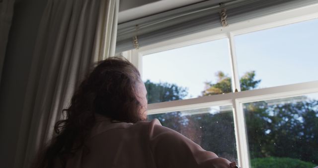 Senior caucasian woman drawing curtains in sunny room and looking out of window. at retirement lifestyle at home.