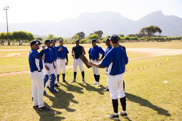 Baseball coach giving instructions to a multi-ethnic team of players on a sunny day. Ideal for use in sports-related content, teamwork and leadership articles, and promotional materials for baseball events and training programs.
