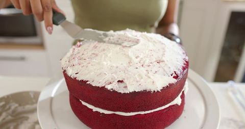 Spreading frosting on two-layer red velvet cake, home baker decorating with spatula