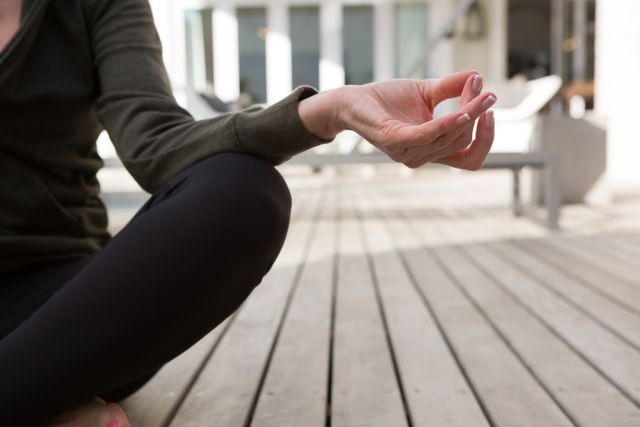 Woman practicing yoga meditation on porch, focusing on hand gesture. Ideal for promoting wellness, mindfulness, and healthy lifestyle. Suitable for use in articles, blogs, and advertisements related to fitness, relaxation, and self-care.
