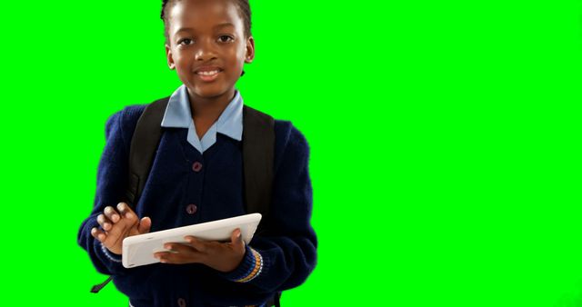 Young girl wearing school uniform and backpack, standing against green screen background, holding tablet. Perfect for educational content, technology in education, digital learning promotions, school projects, or childhood education materials.