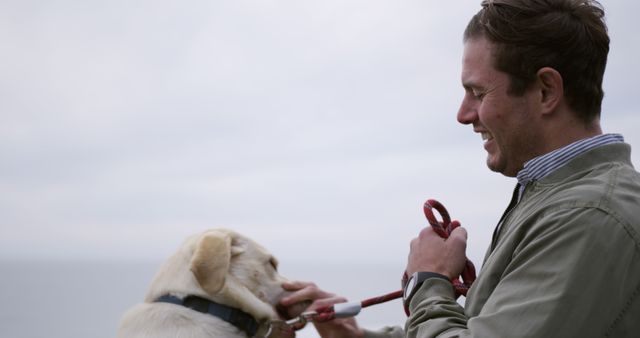 This image shows a man smiling and holding the leash of a Labrador dog on a cloudy day outdoors. Perfect for use in content related to pet care, outdoor activities, companionship, and lifestyle blogs.