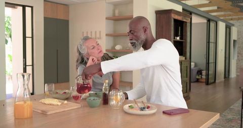 Mature couple sharing breakfast, man pouring red tea in sunlit open-plan kitchen