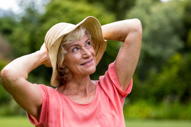 Smiling senior woman in hat standing at yard 