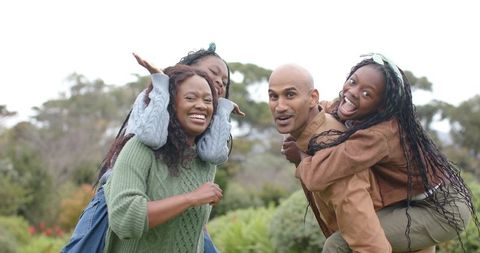 Parents Giving Piggyback Rides to Daughters Laughing in Park Family Outdoor Fun