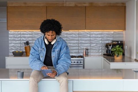 African american man sitting on kitchen island using tablet with headphones, remote work